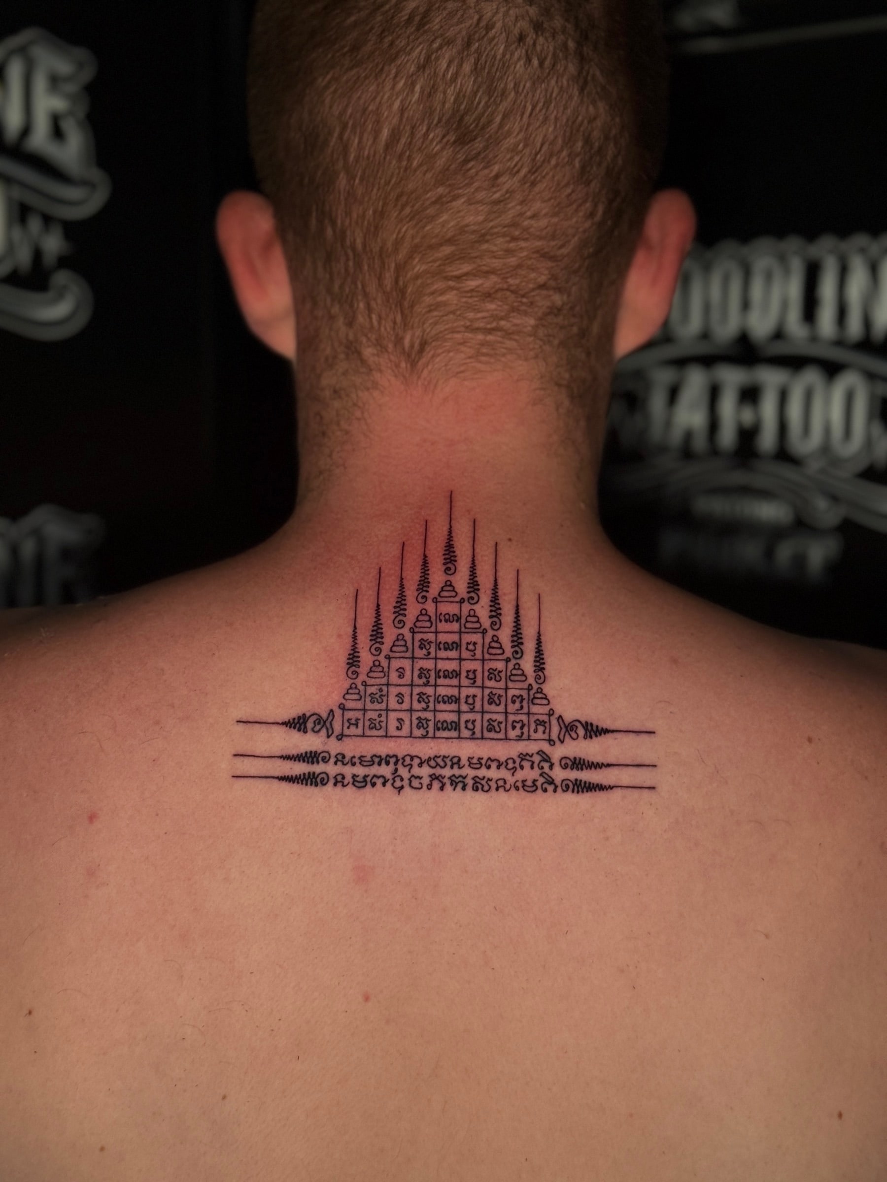 Gao Yord (Nine Spires) Sak Yant with a geometric pyramid grid of Khom script and nine peaked unalomes centered on the upper back at Bloodline Tattoo Phuket.