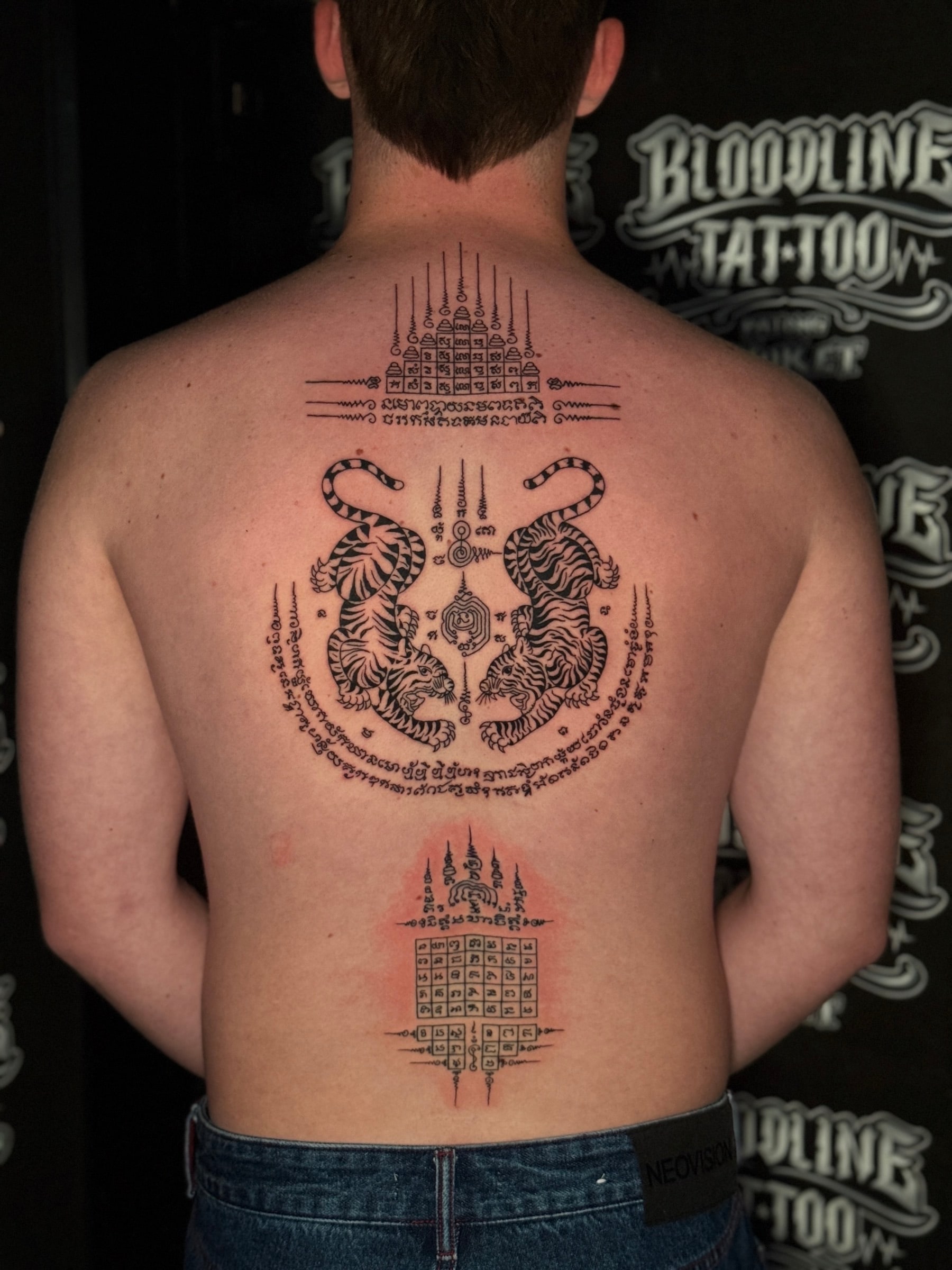 Upper-back Sak Yant composition with Gao Yord nine spires, Suea Koo twin tigers, and a lower geometric yantra grid with Khom script at Bloodline Tattoo Phuket.