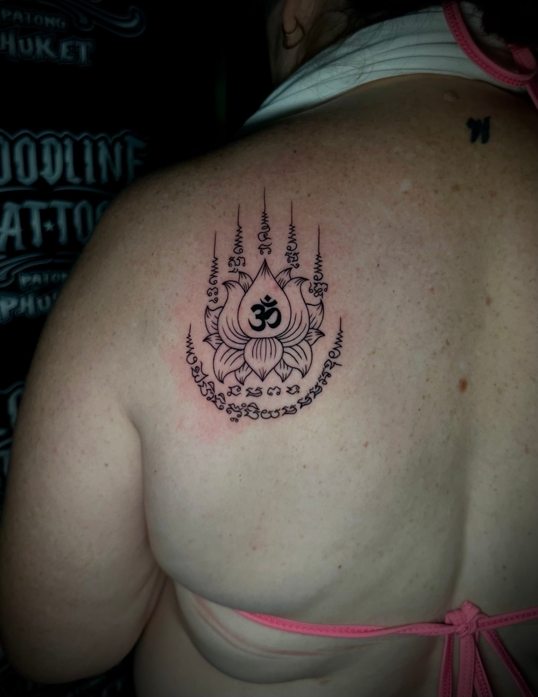 Hah Taew (Five Lines) Sak Yant with five Khom script columns, unalomes, and a central lotus flower bearing an Om symbol on the left shoulder blade at Bloodline Tattoo Phuket.