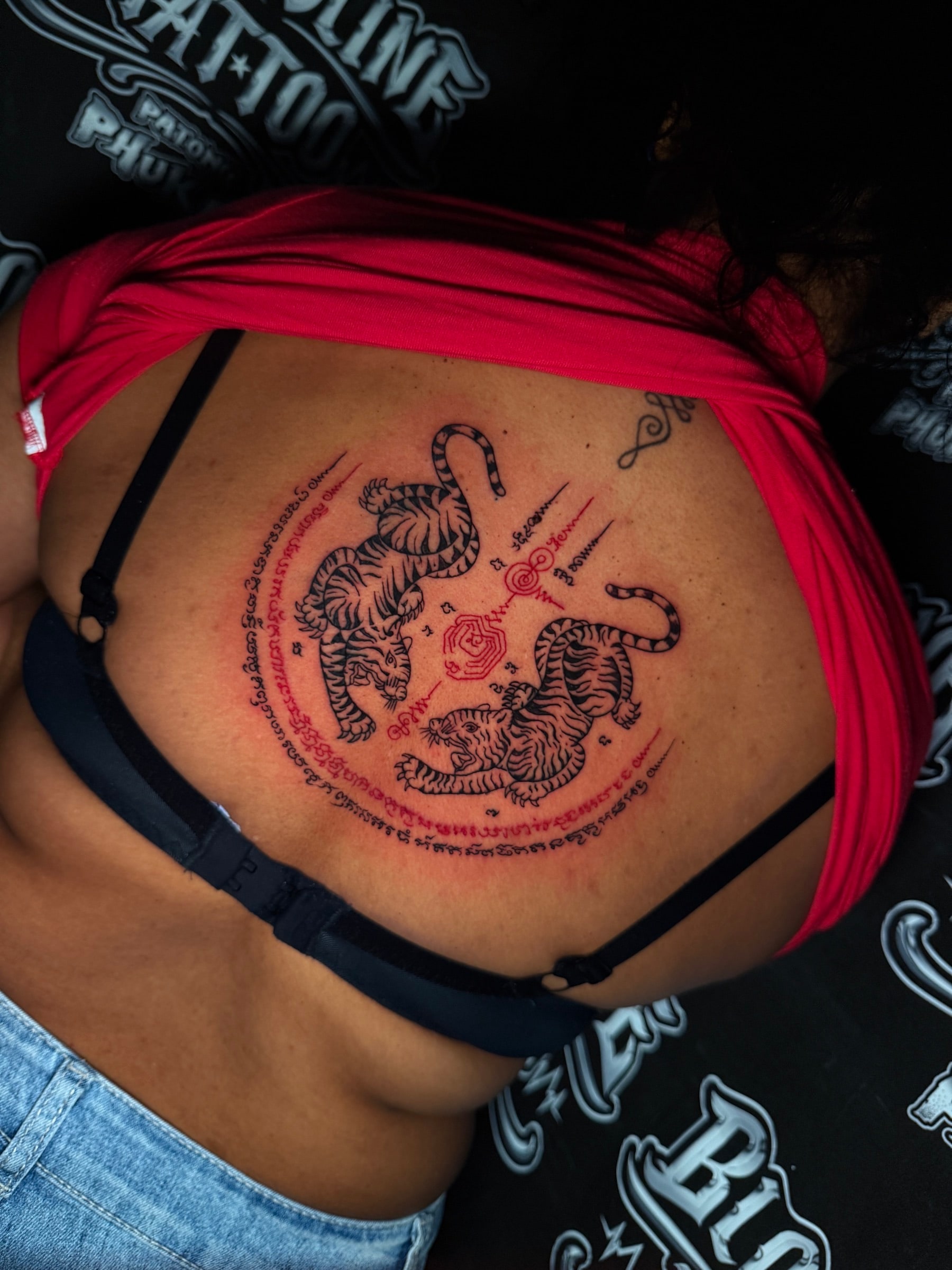 Suea Koo (Twin Tigers) Sak Yant with black-ink tigers and red Khom script in a circular yantra on the upper back at Bloodline Tattoo Phuket.