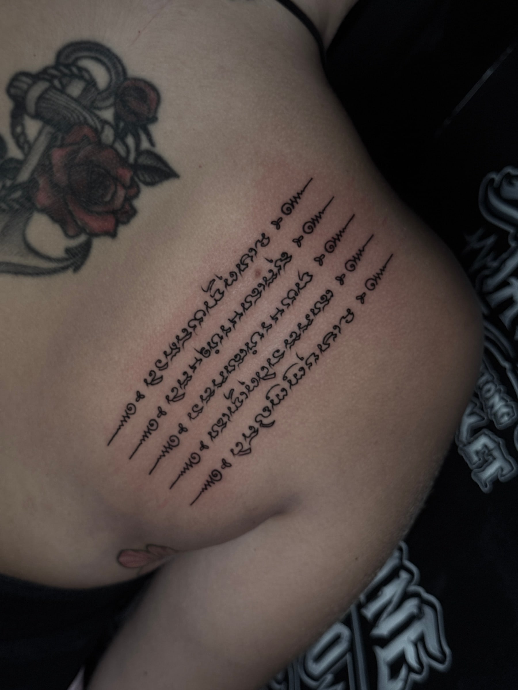 Hah Taew (Five Sacred Lines) Sak Yant with five vertical Khom script rows and unalome symbols on the ribcage at Bloodline Tattoo Phuket.