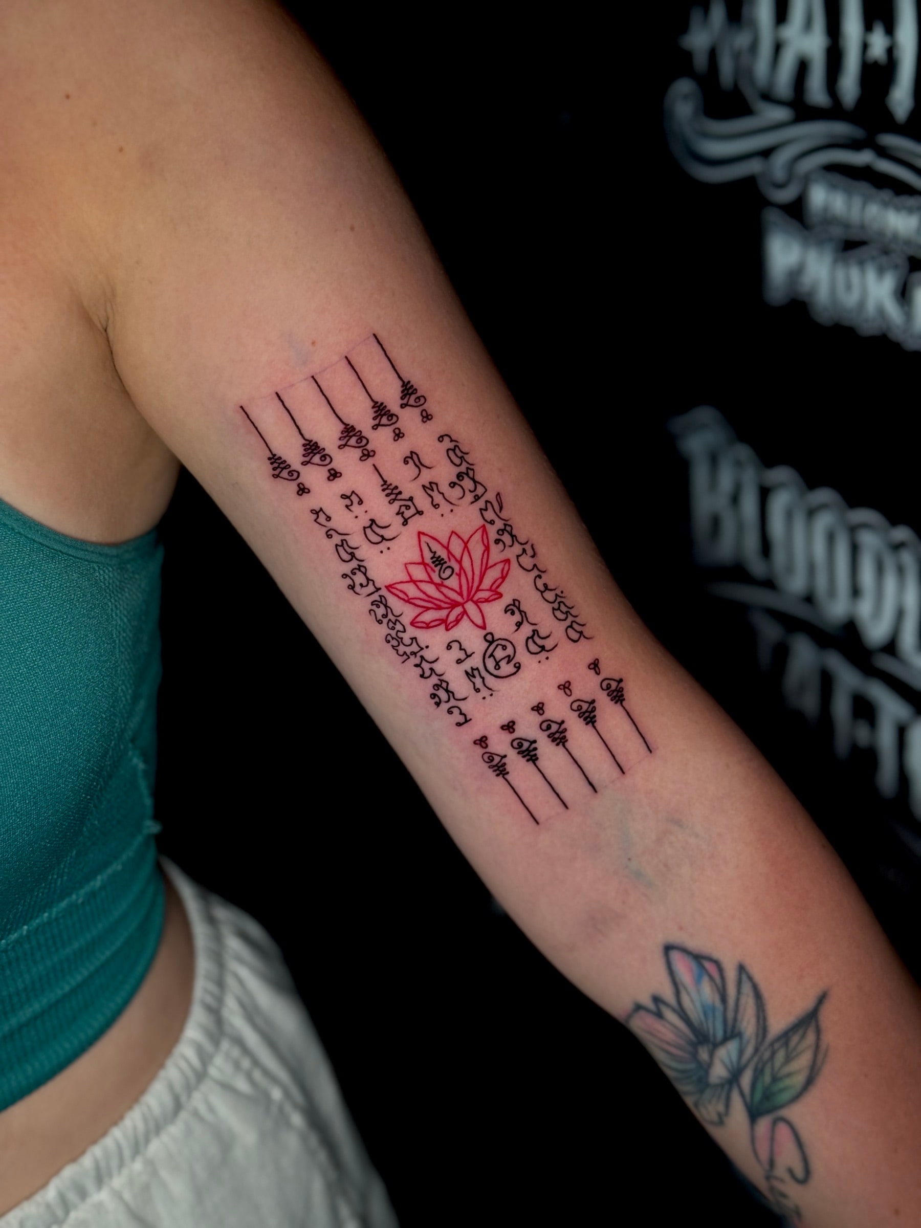 Hah Taew (Five Lines) Sak Yant with five Khom script columns framing a vibrant red lotus flower on the inner forearm at Bloodline Tattoo Phuket.