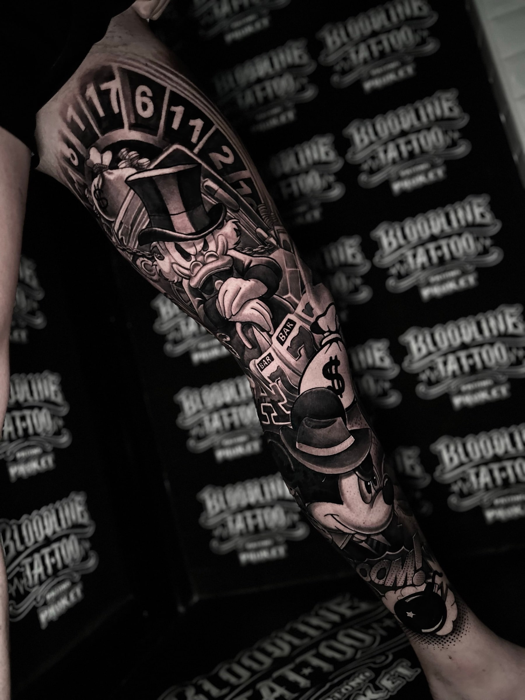 Chicano leg tattoo with Scrooge McDuck, fedora Mickey Mouse, a roulette wheel, slot reels, money bags, and a cartoon bomb at Bloodline Tattoo Phuket.