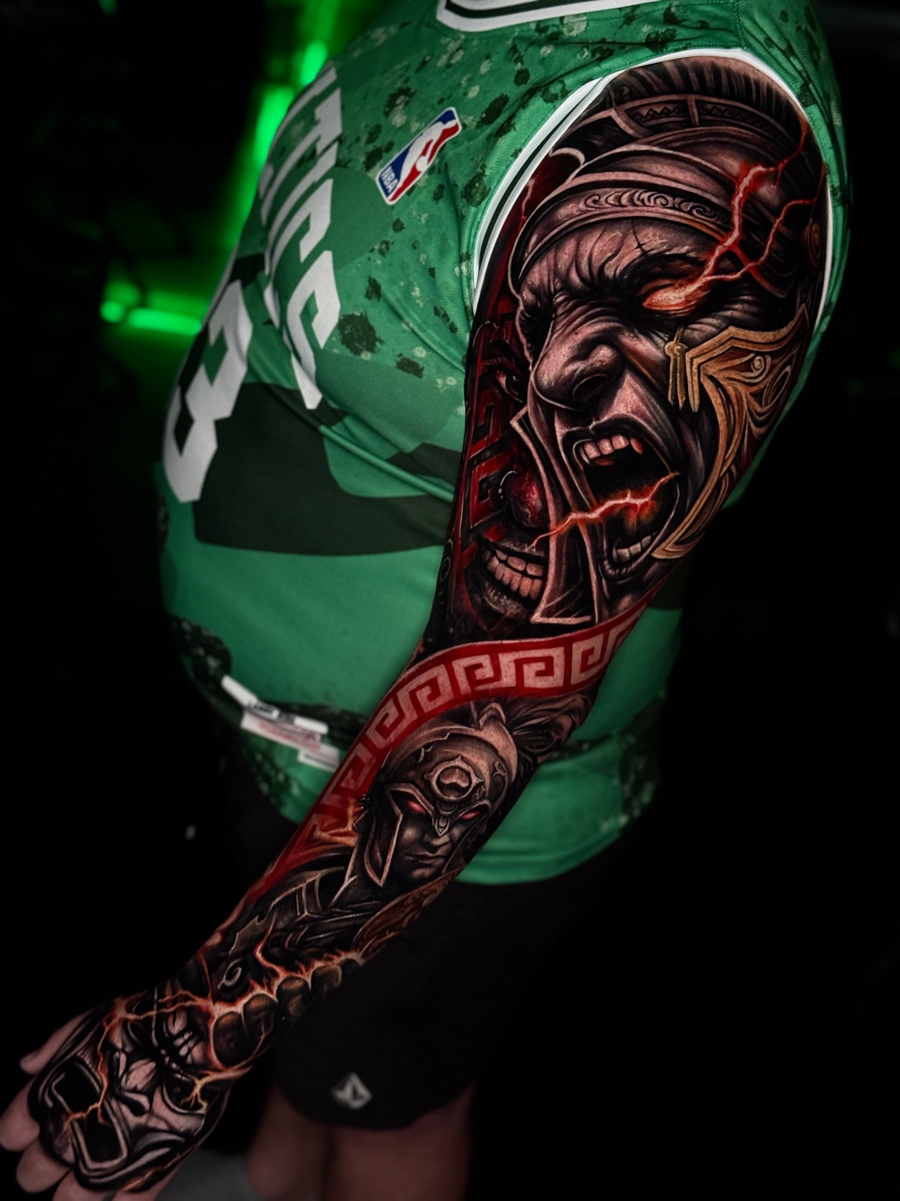 Full-sleeve colour tattoo of a screaming warrior with glowing red lightning, a Spartan helmet figure, and a red Greek key band extending onto the hand at Bloodline Tattoo Phuket.