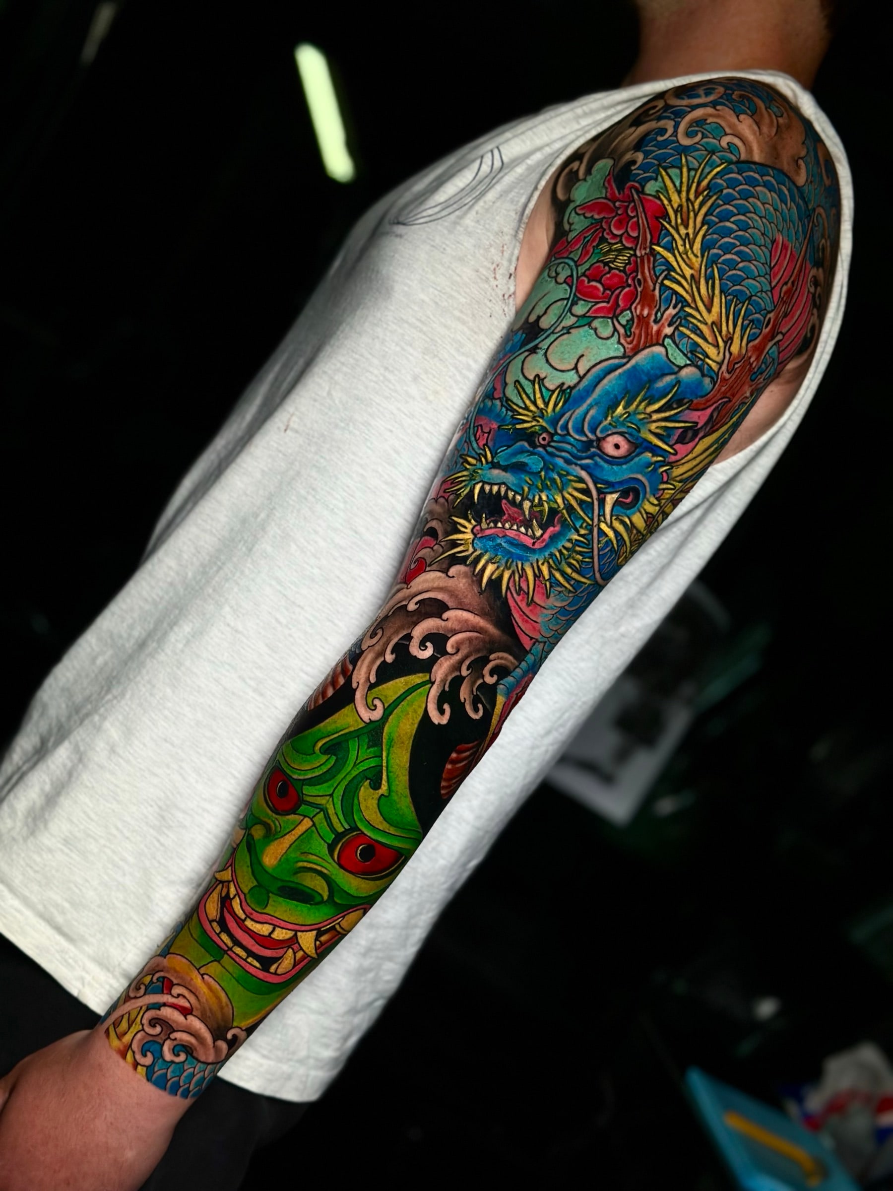 Japanese Irezumi colour sleeve with a blue dragon, a green Hannya mask, and swirling wave backgrounds at Bloodline Tattoo Phuket.