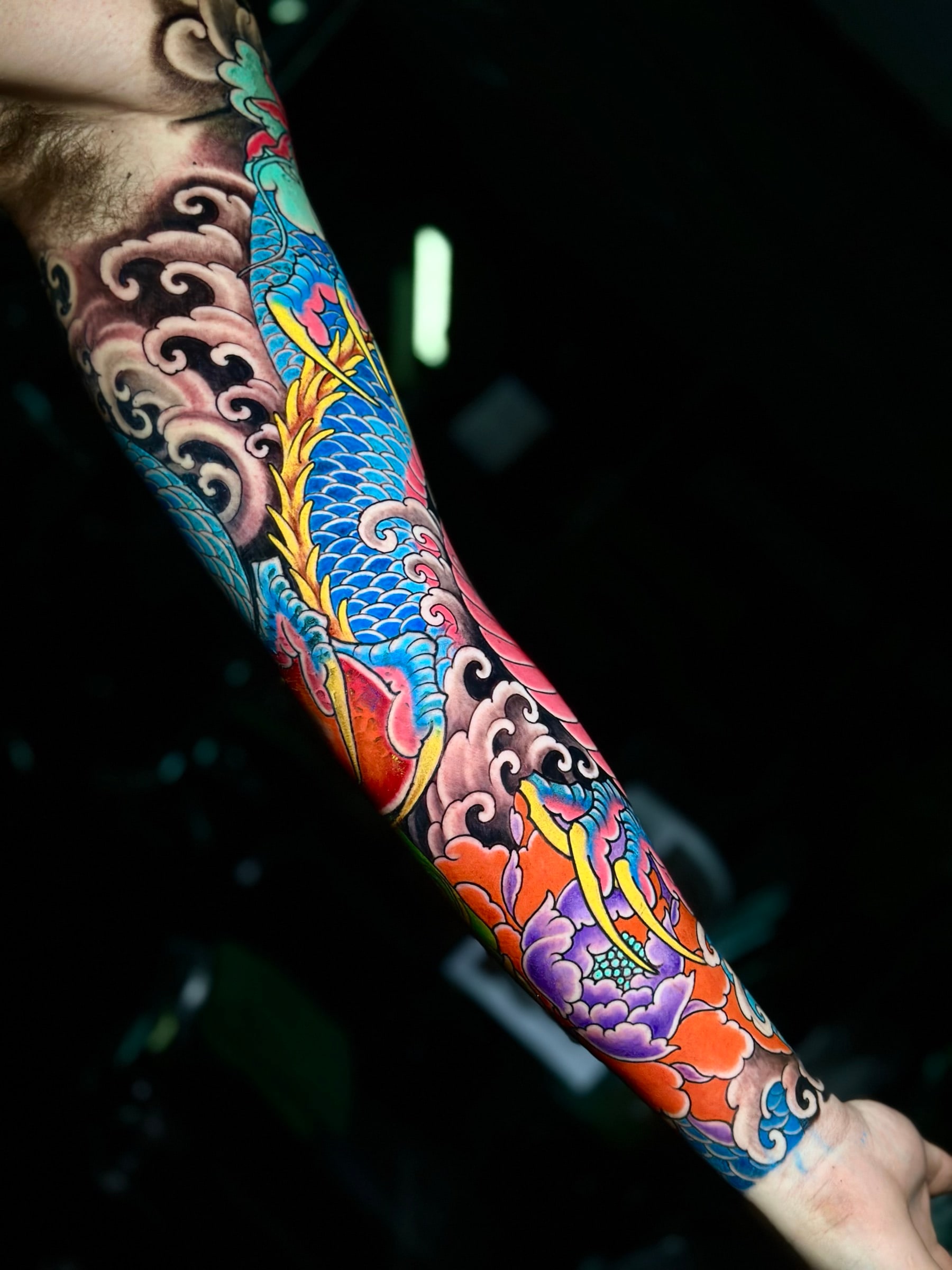 Vibrant Japanese colour sleeve featuring a coiled blue dragon, a purple peony, and traditional black wind-bar shading at Bloodline Tattoo Phuket.