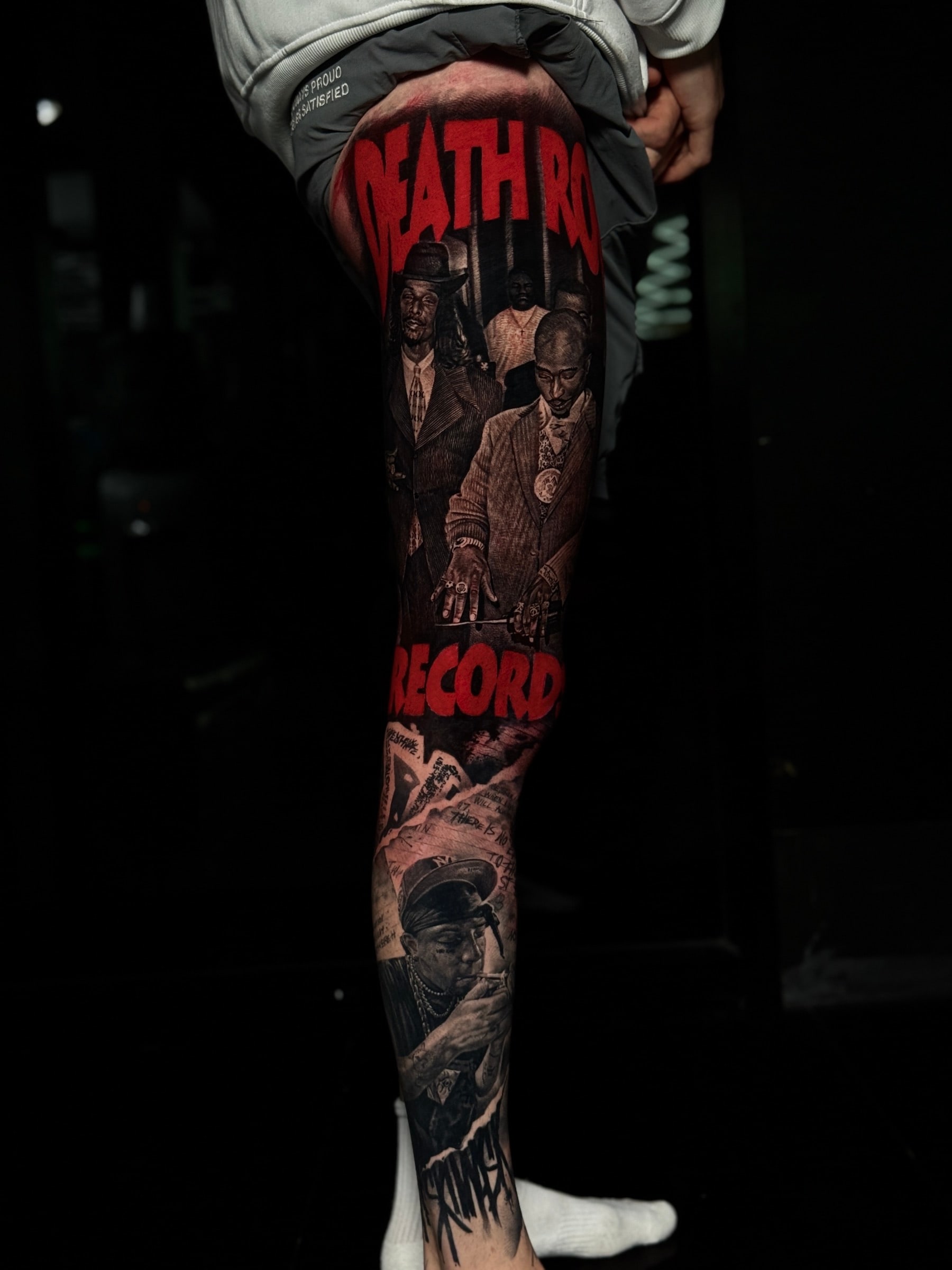 Colour realism leg tattoo of Death Row Records with red block lettering and portraits of Snoop Dogg and Tupac Shakur at Bloodline Tattoo Phuket.