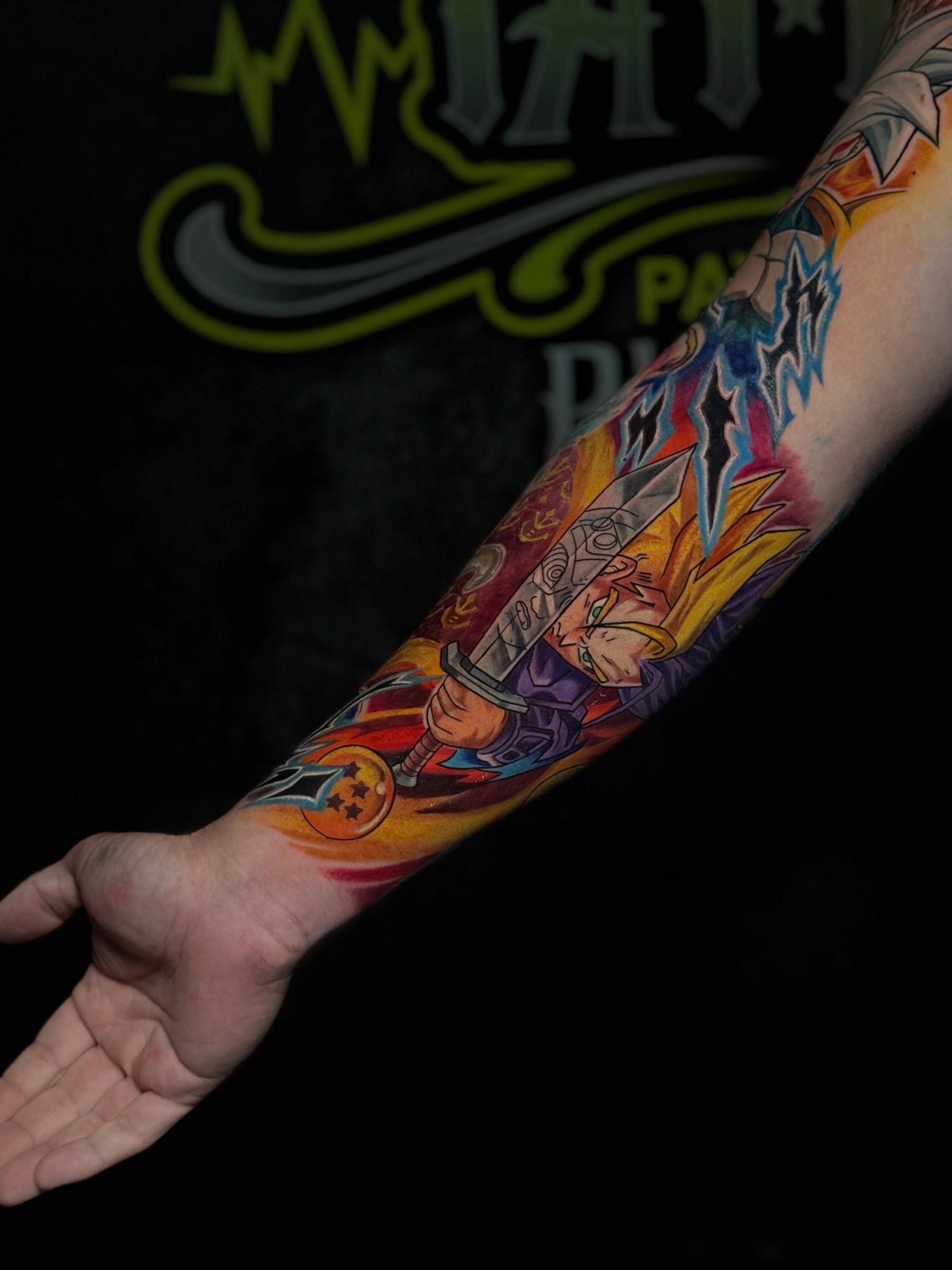 Colour forearm tattoo of Super Saiyan Trunks wielding his sword beside a four-star Dragon Ball with blue energy effects at Bloodline Tattoo Phuket.