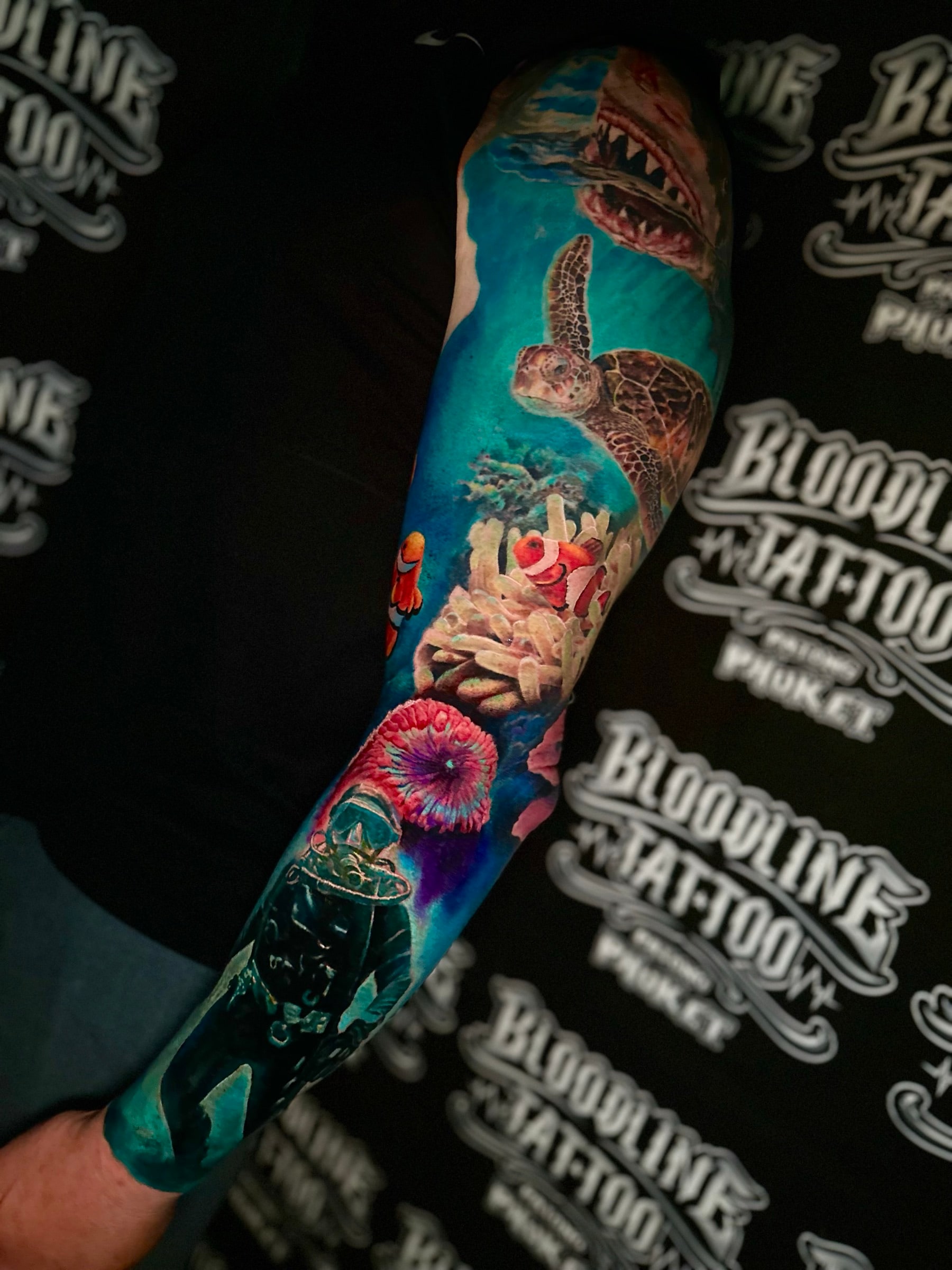 Underwater colour sleeve with a shark, sea turtle, clownfish in anemone, and a scuba diver in deep blue water at Bloodline Tattoo Phuket.
