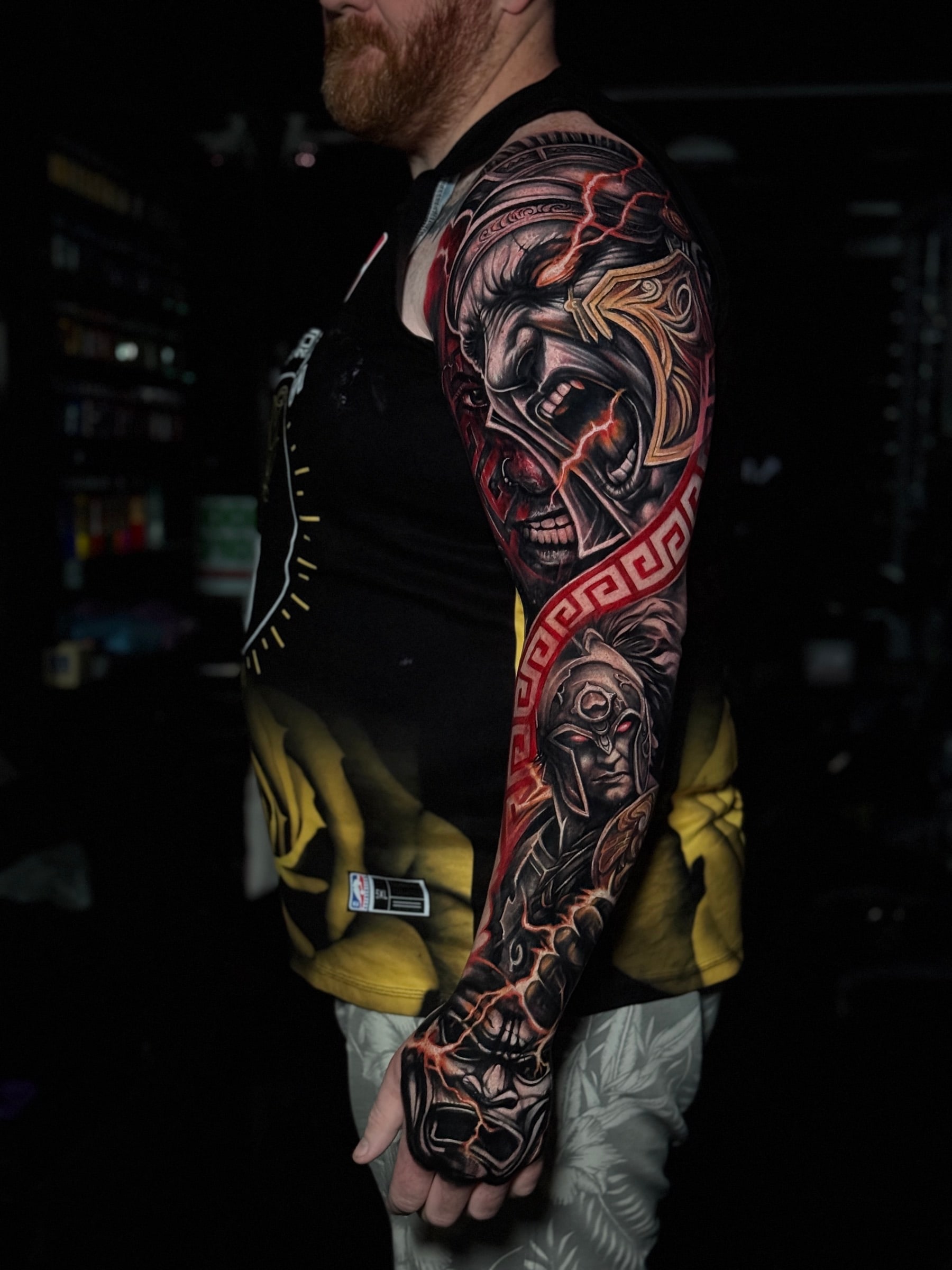 Colour full sleeve of a screaming warrior with red lightning bolts, a Spartan helmet portrait, and a red Greek key band on the hand at Bloodline Tattoo Phuket.