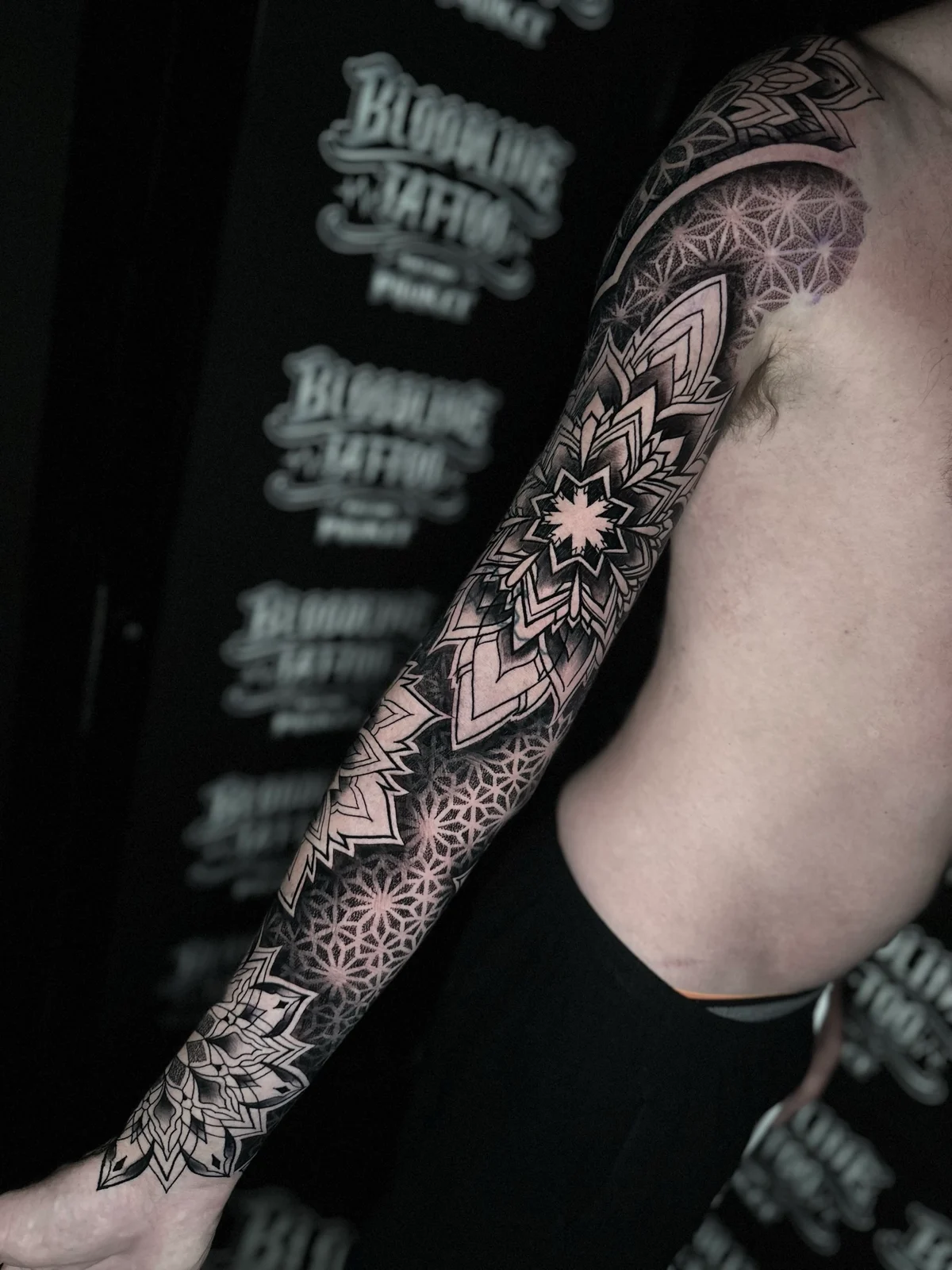 Geometric mandala dotwork full sleeve with large elbow and wrist mandalas set in a repeating sacred-geometry star grid at Bloodline Tattoo Phuket.