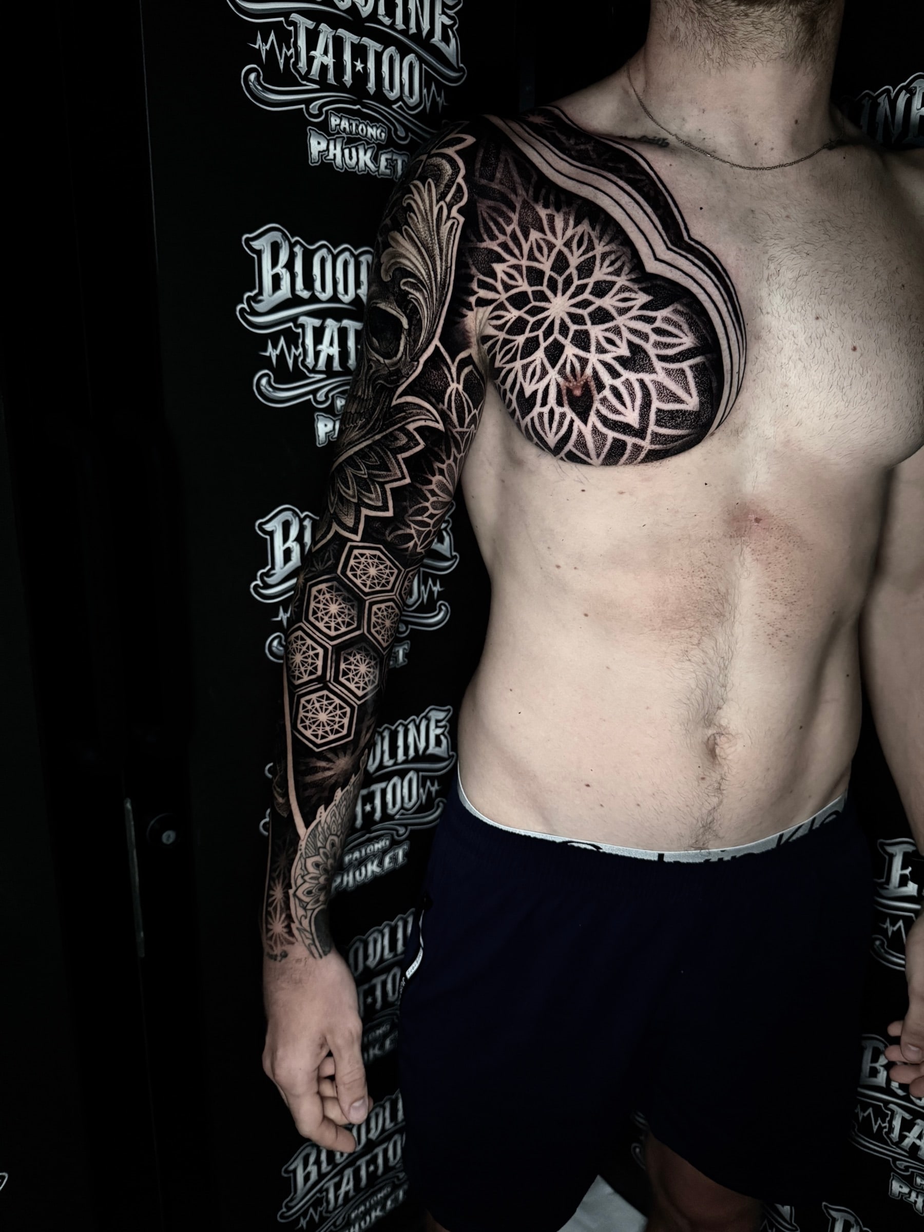 Chest and arm mandala tattoo with a large pectoral lotus mandala flowing into a honeycomb geometric forearm sleeve at Bloodline Tattoo Phuket.