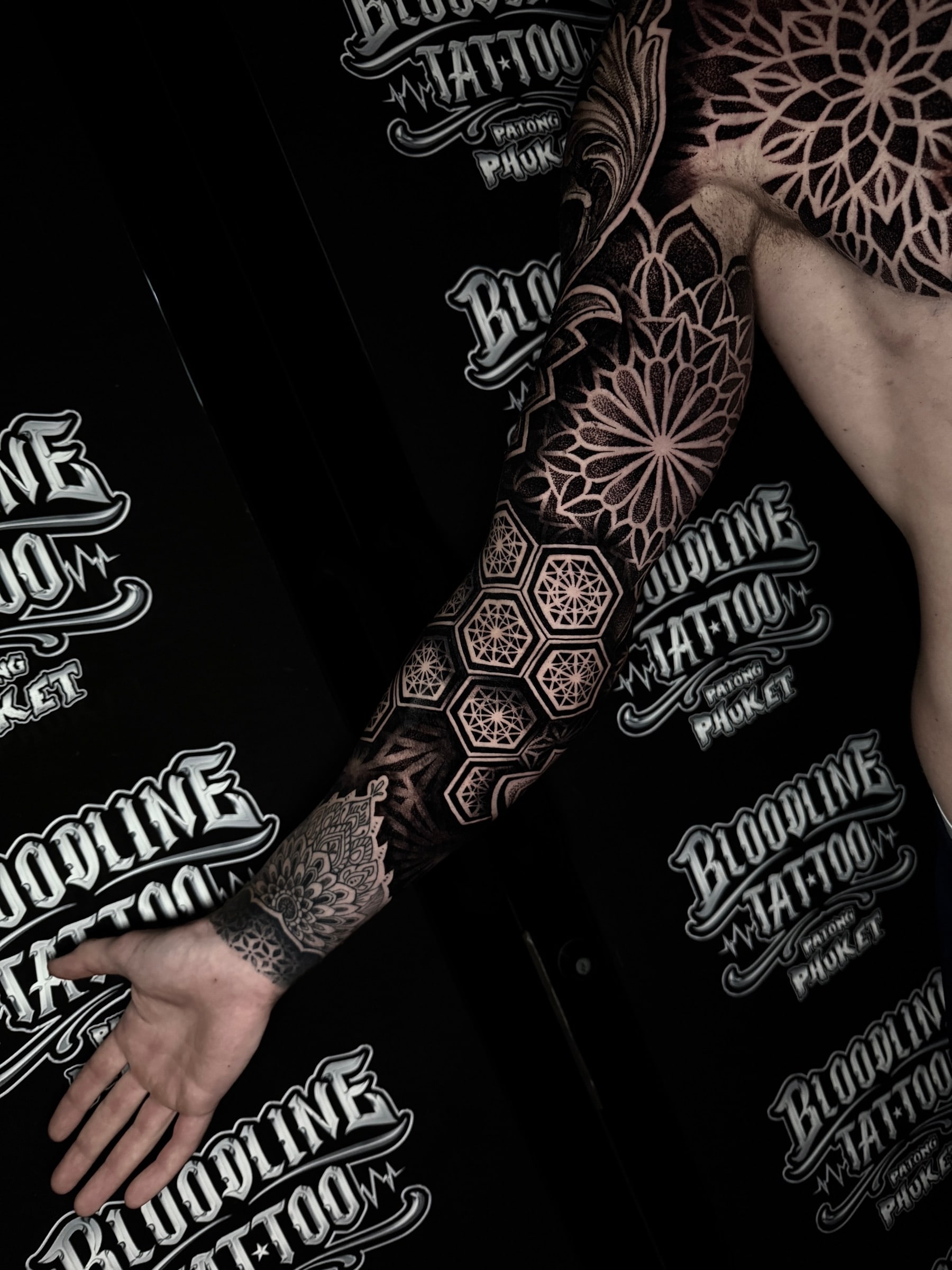 Chest mandala and full arm sleeve with dotwork lotus patterns, overlapping shoulder mandalas, and hexagonal forearm geometry at Bloodline Tattoo Phuket.