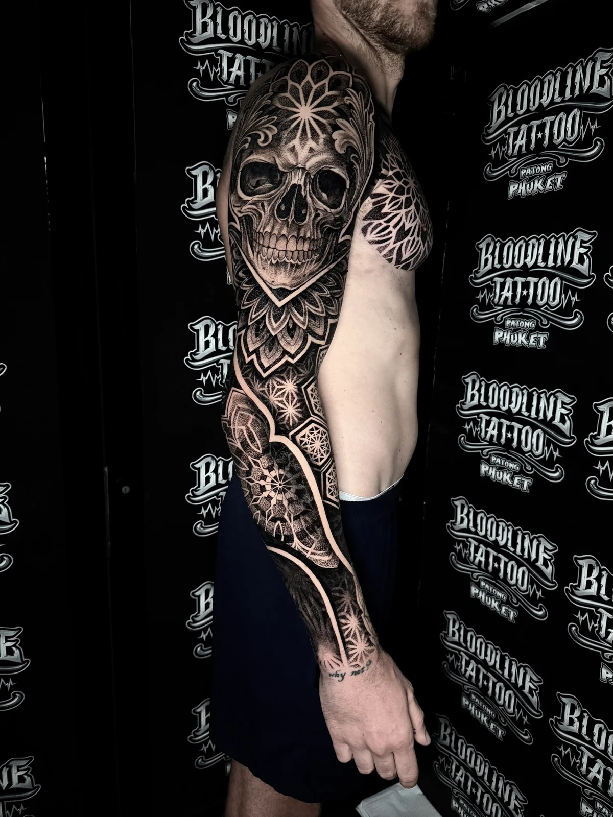 Blackwork mandala sleeve with a realistic skull bearing a forehead mandala, chest filigree, and star geometric wrist patterns at Bloodline Tattoo Phuket.