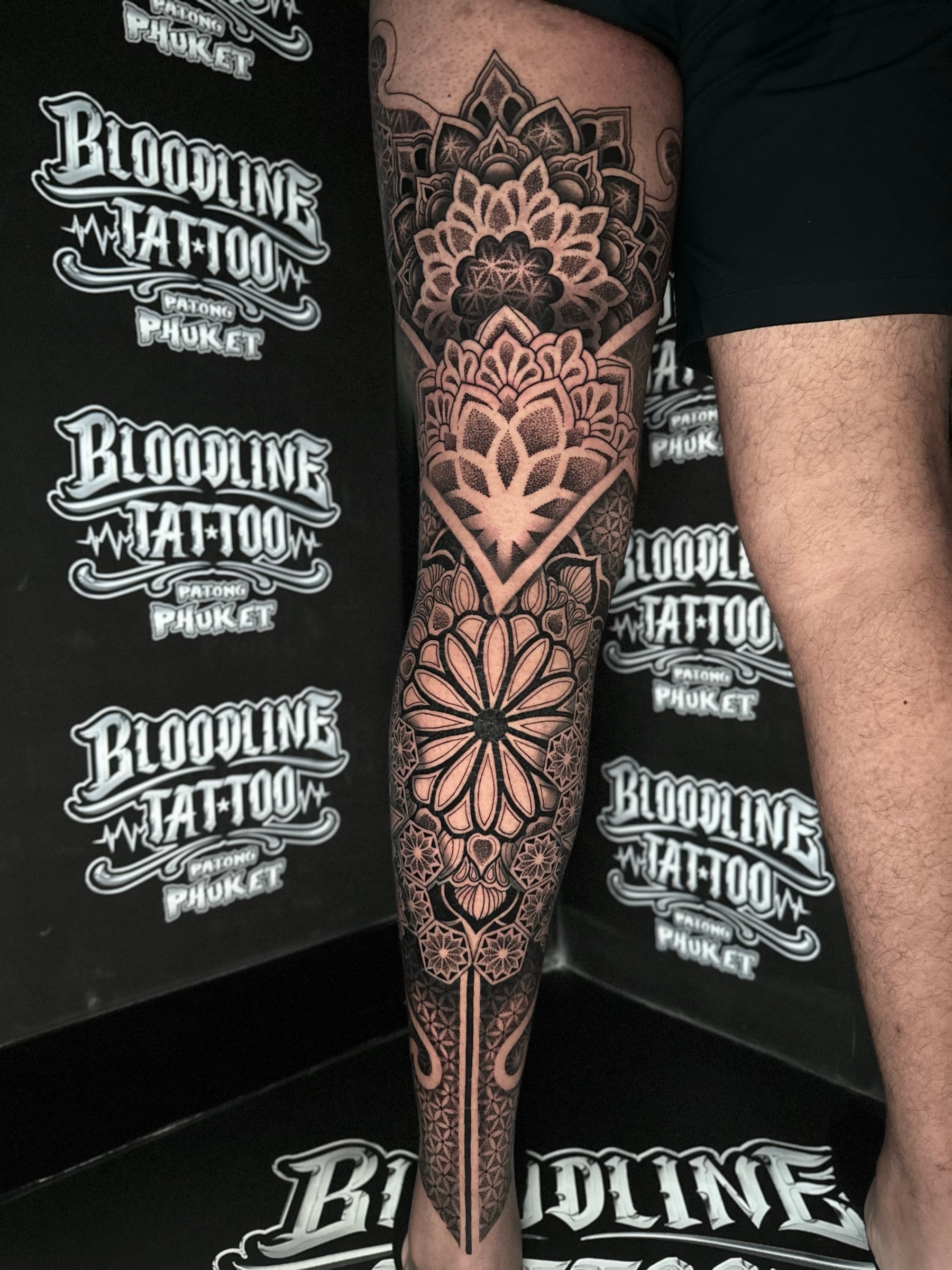 Stacked blackwork leg mandalas with a thigh lotus, a diamond-framed knee floral, and a circular shin mandala with ankle geometry at Bloodline Tattoo Phuket.