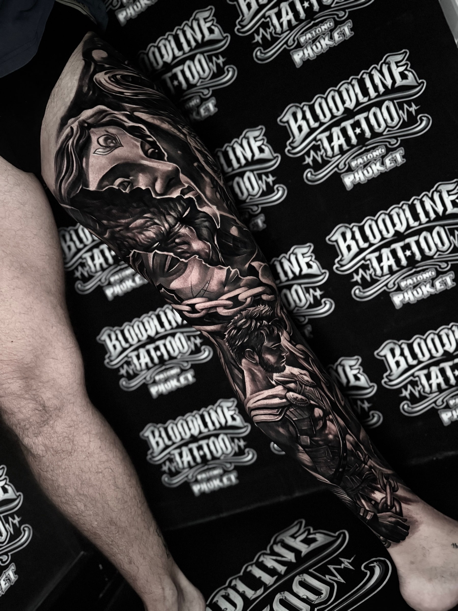Detailed black and grey realism full leg sleeve tattoo featuring a woman with a third eye, heavy chains, and a gladiator warrior in armor at Bloodline Tattoo Phuket.