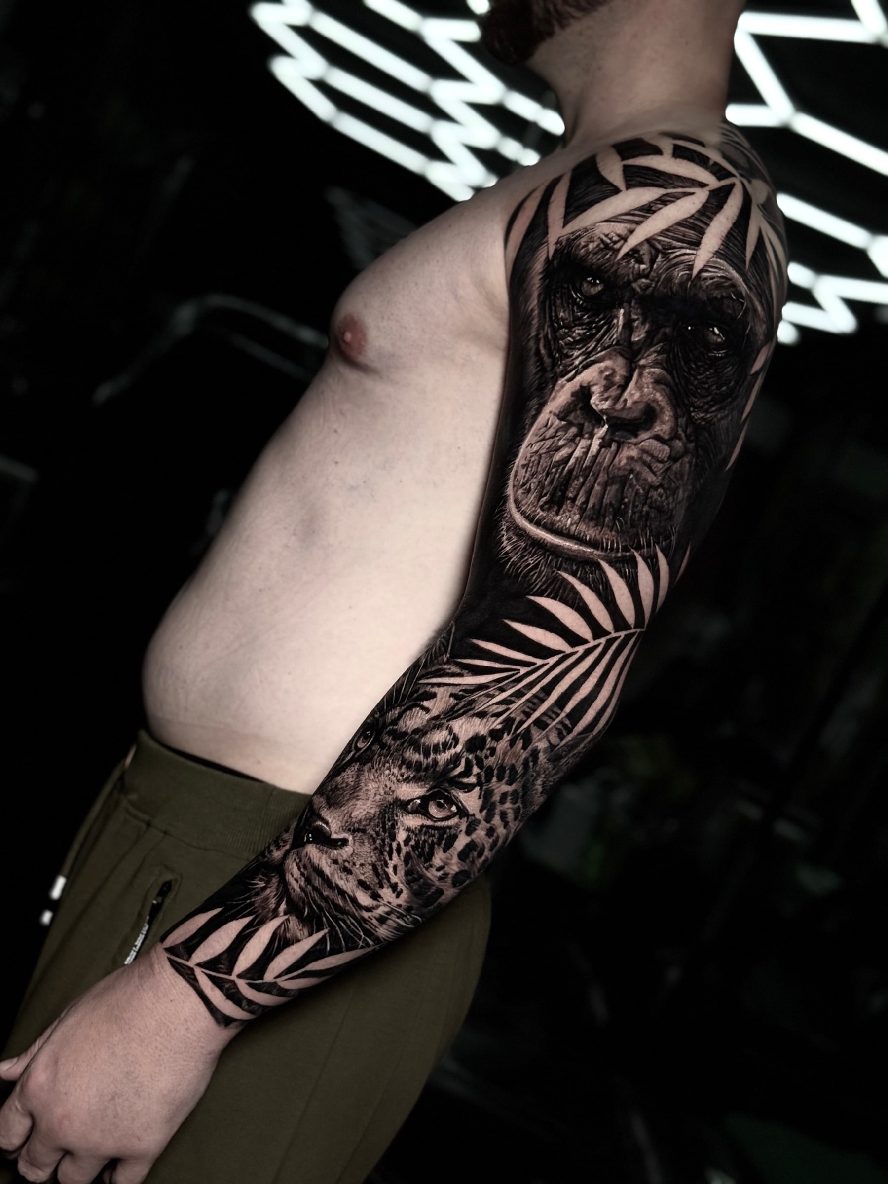 Detailed black and grey realism full sleeve tattoo featuring realistic chimpanzee and leopard portraits framed by tropical palm fronds at Bloodline Tattoo Phuket.